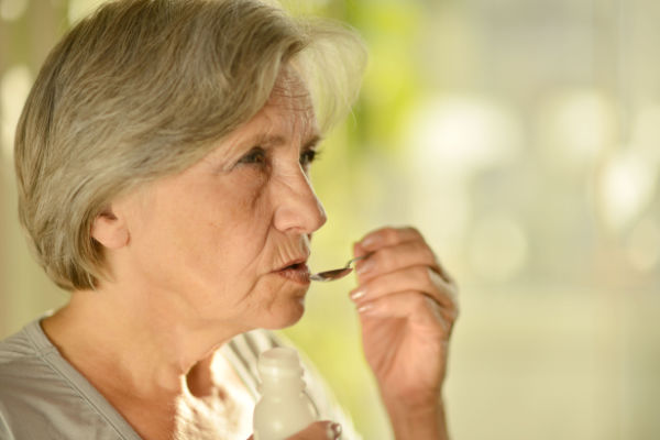 A senior woman carefully and cautiously holds a spoon to her mouth.