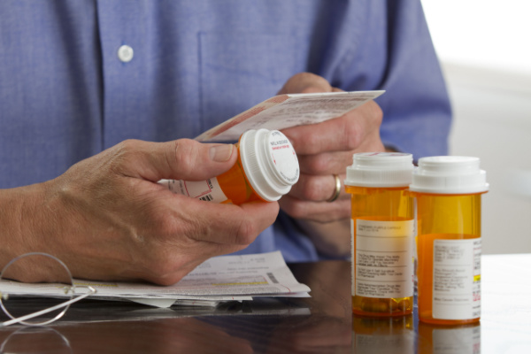 A man holds a prescription medication bottle as he reads prescription information. 