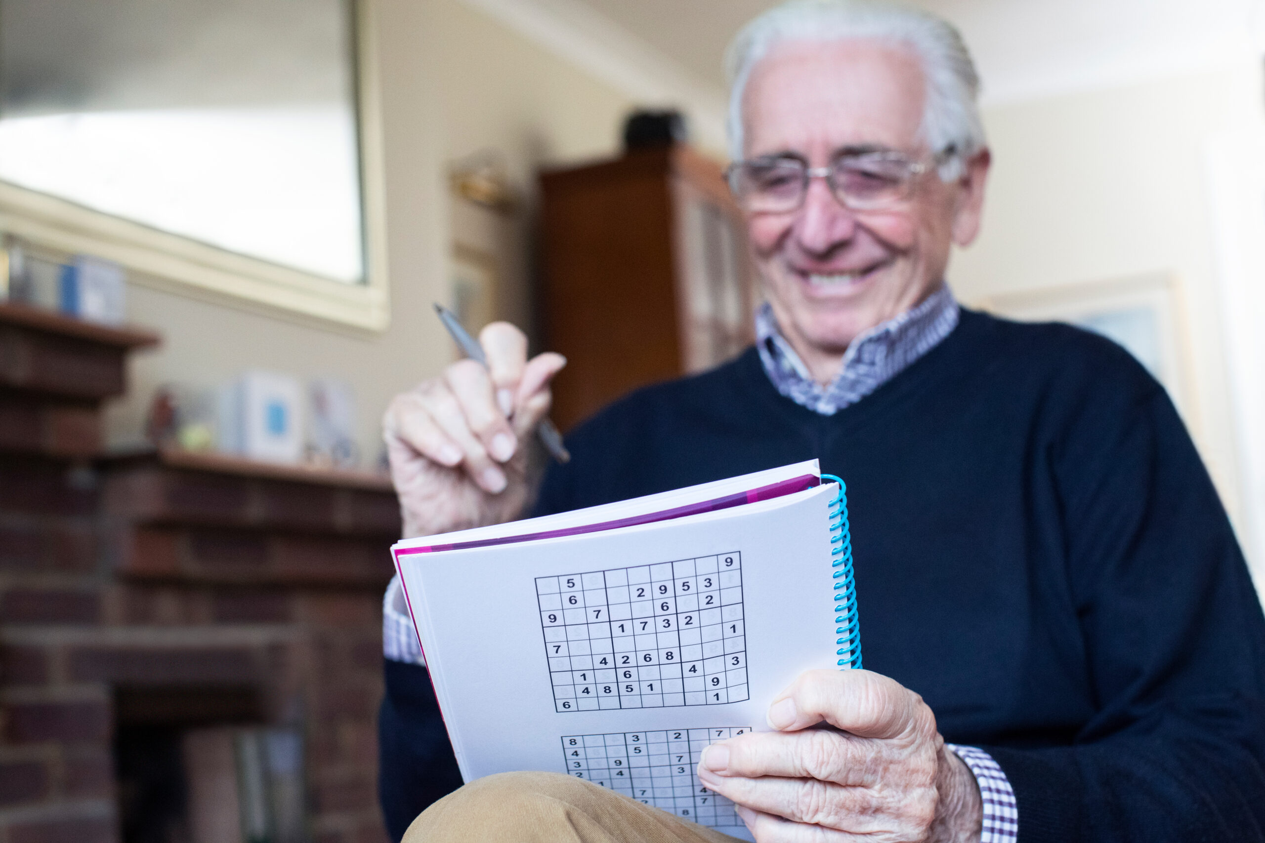 A man smiles as he works on a Sudoku puzzle.