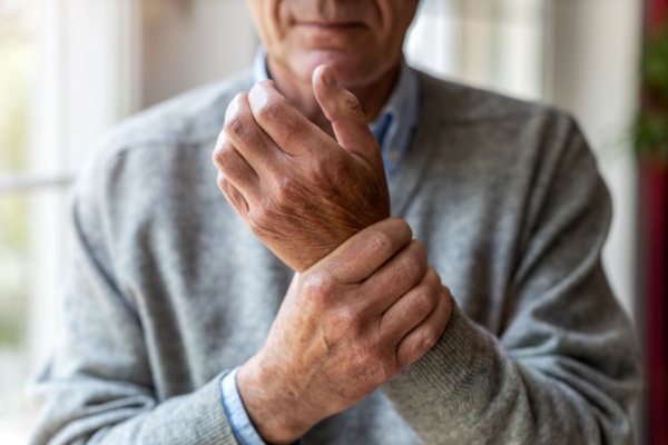 A senior man holds his wrist, which appears to be sore.